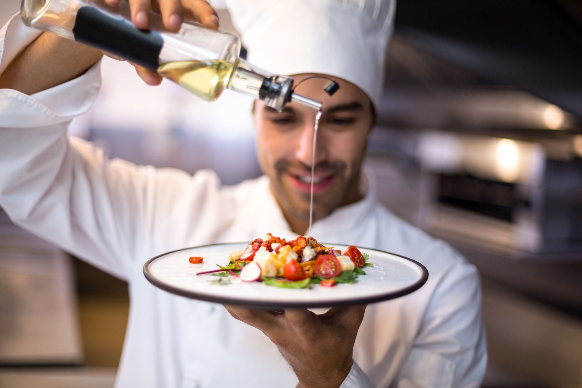 Handsome chef pouring olive oil on meal